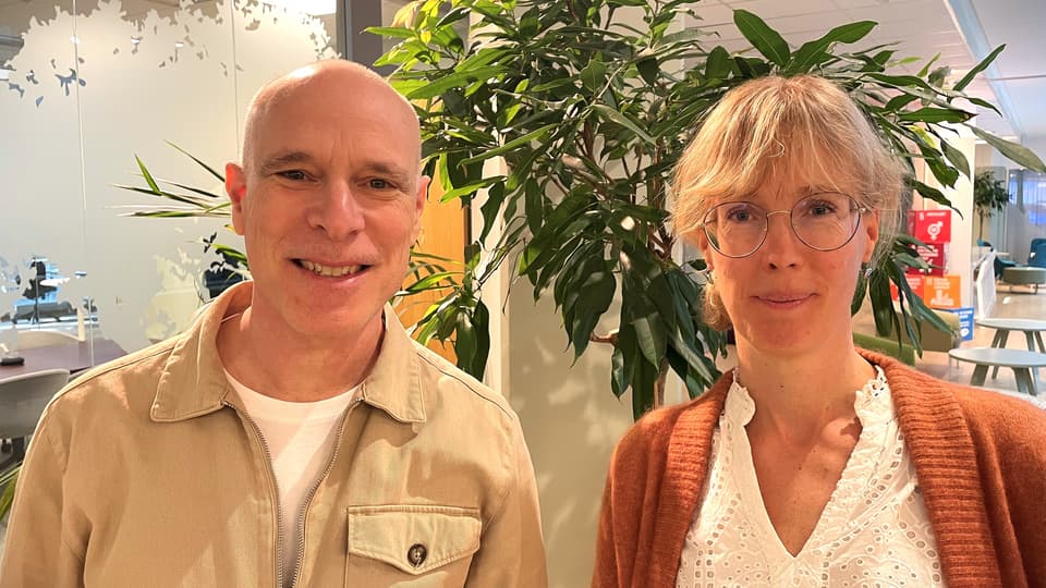 En bild på en man och kvinna från Folkhälsomyndigheten. Mannen står till vänster och kvinnan till höger. I bakgrunden finns et kontorslandskap och gröna växter